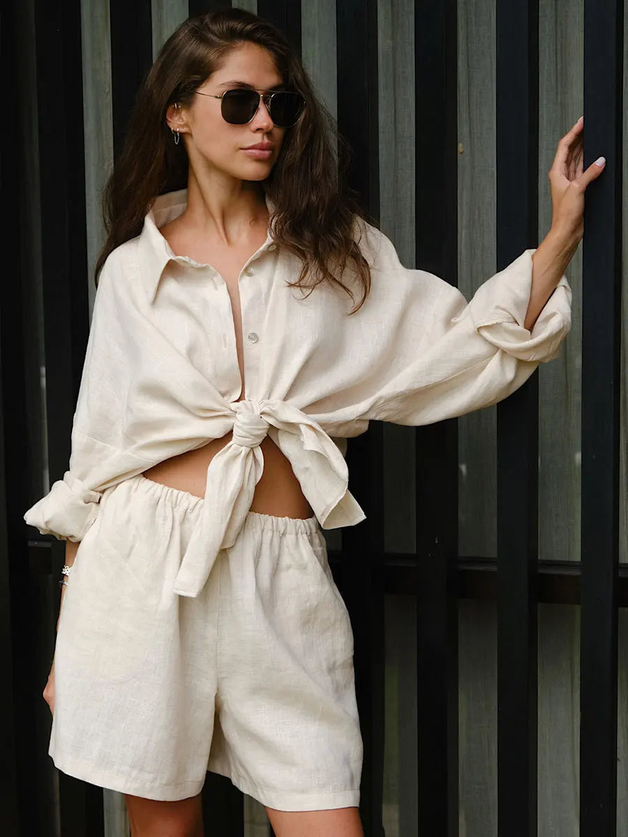 A female model wearing a beige cotton casual wear outfit with a top and shorts, featuring a bow tie detail on the top.