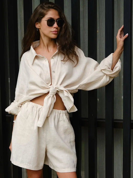 A female model wearing a beige cotton casual wear outfit with a top and shorts, featuring a bow tie detail on the top.